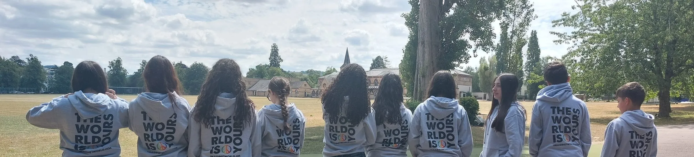 Imagine1world students seen from behind on the Cheltenham College field, with the college buildings beyond